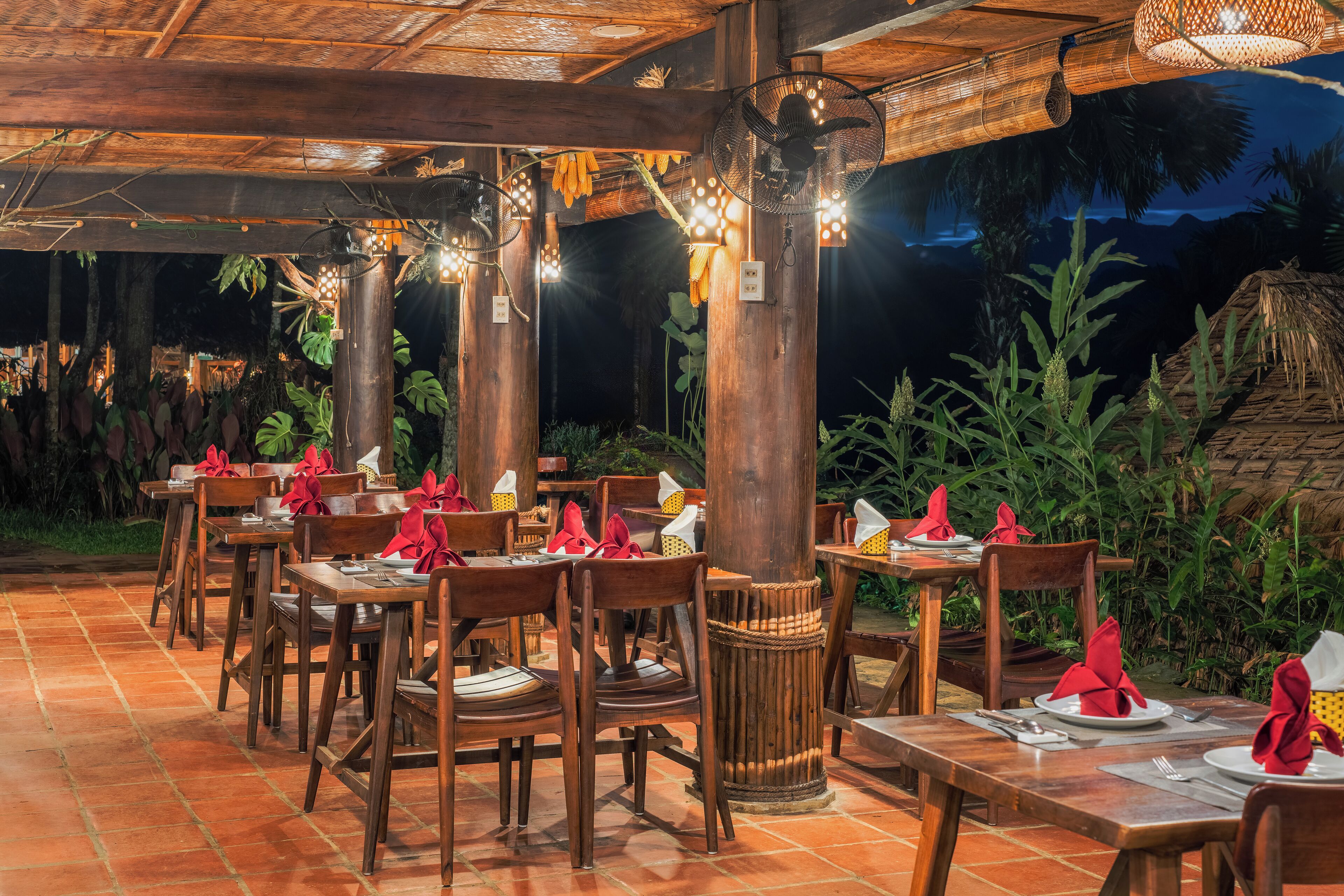 Ein Restaurant im Freien mit Holztischen und -stühlen, an jedem Tisch Geschirr, Besteck und Servietten.