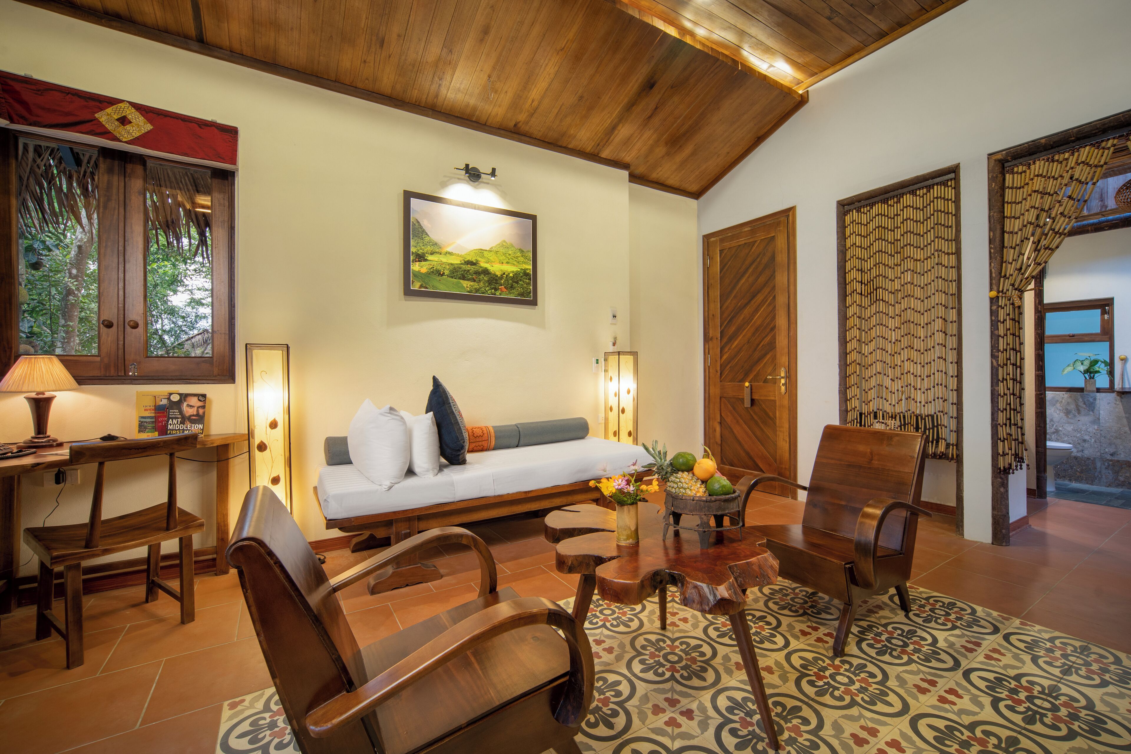 A cozy living room with a wooden ceiling, a sofa with cushions, a coffee table with fruit, and a patterned rug.