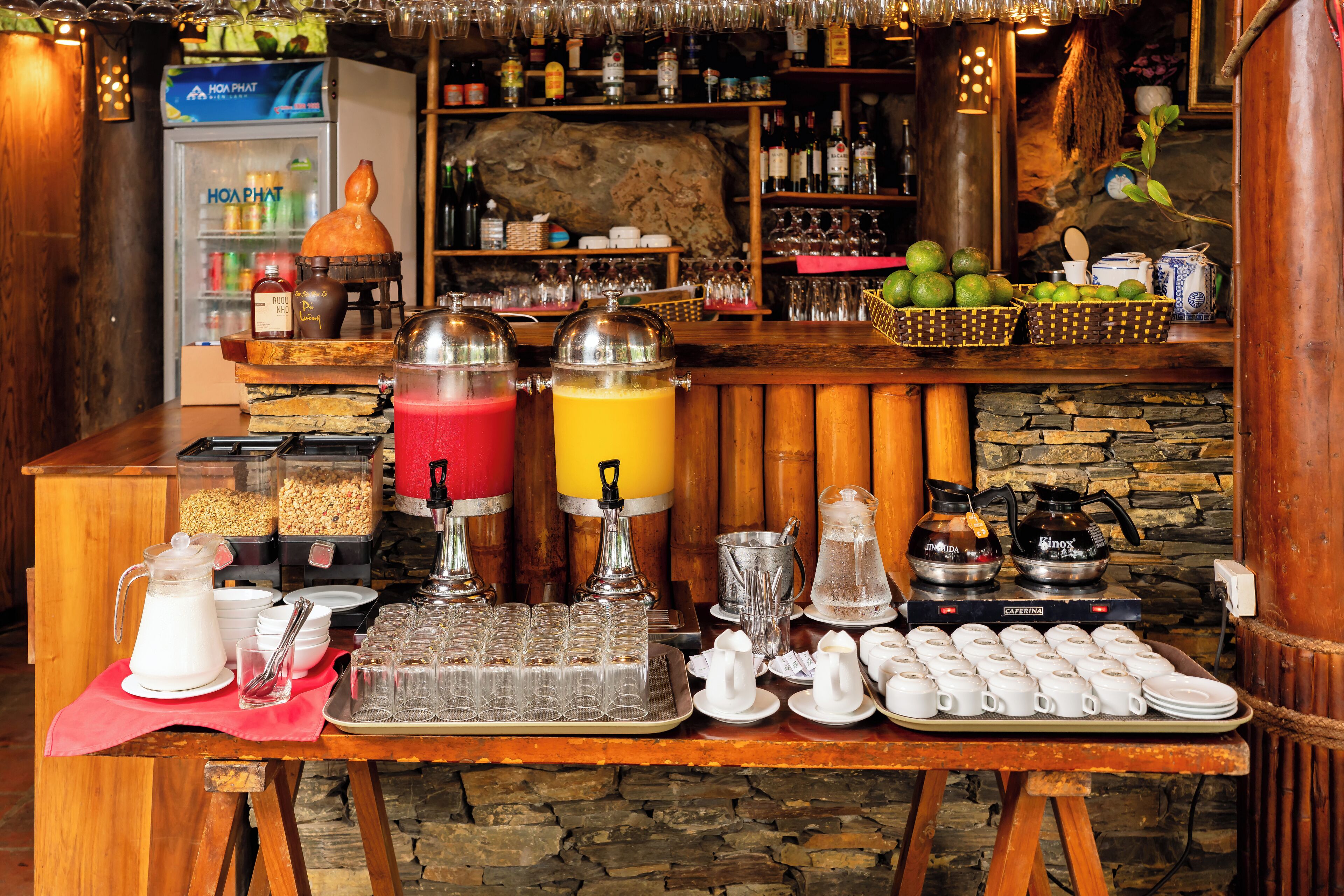 En morgenmadsbuffet med forskellige mad- og drikkevarer, heriblandt en kaffemaskine, juiceautomater og en frugtkurv.