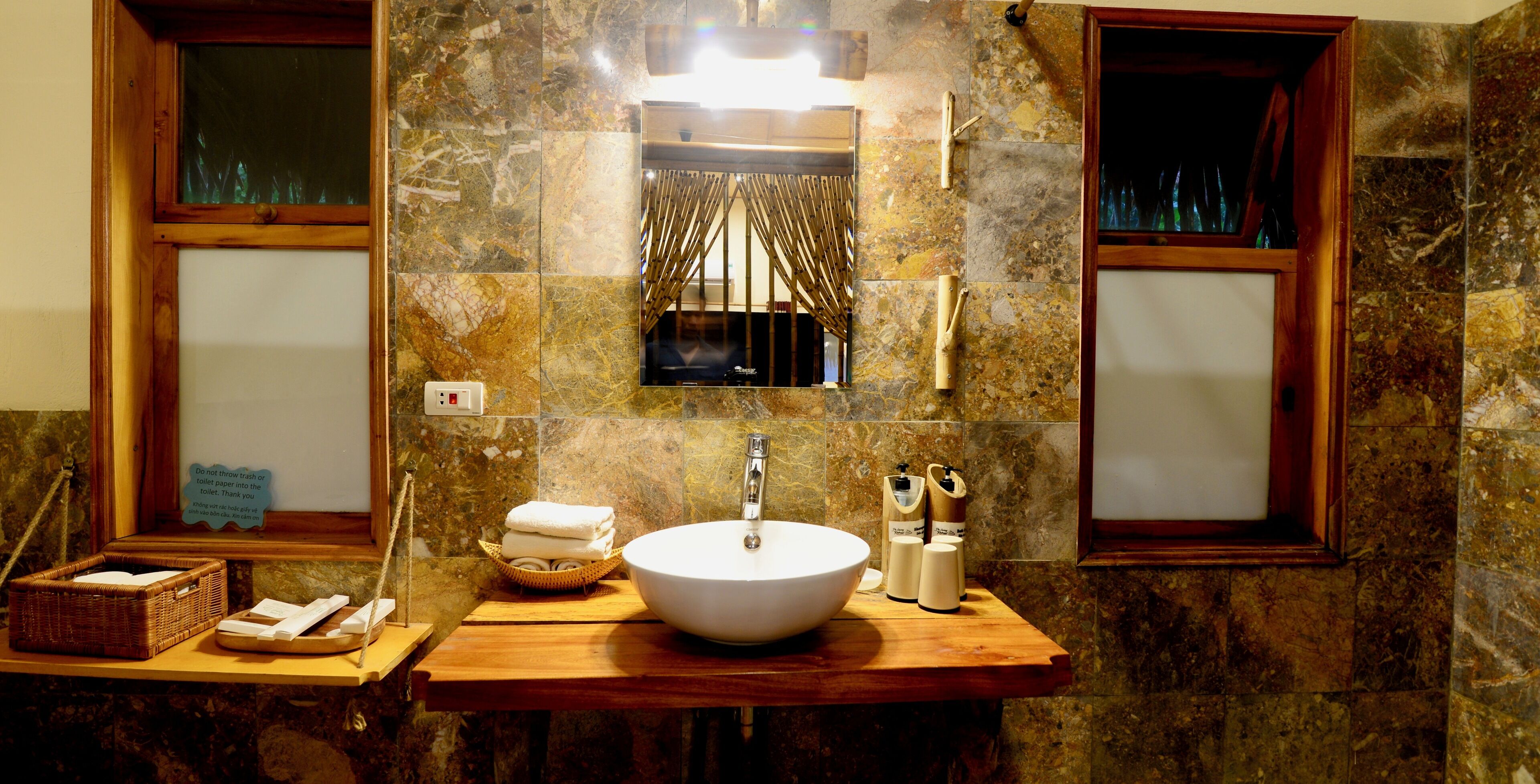 A bathroom with a marble wall, a wooden vanity, a white sink, and a mirror.