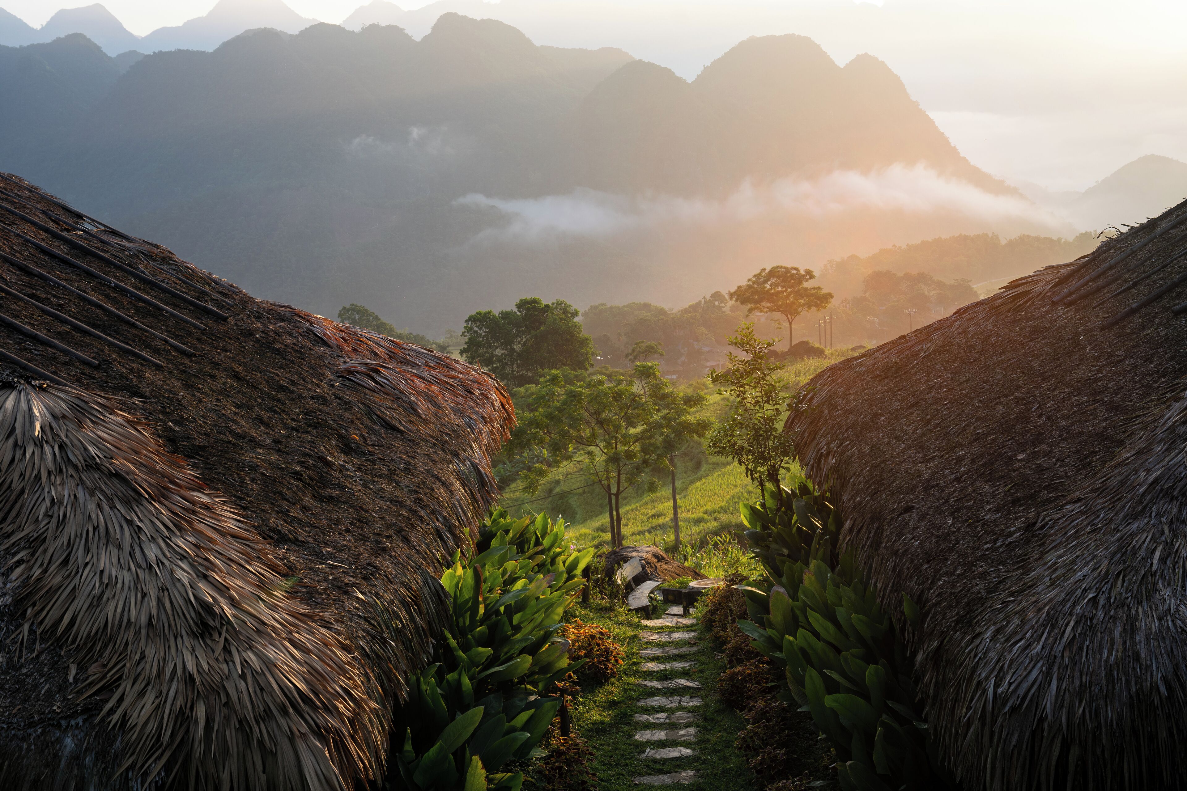 A pathway leading through a mountainous area with thatched-roof huts and lush greenery.
