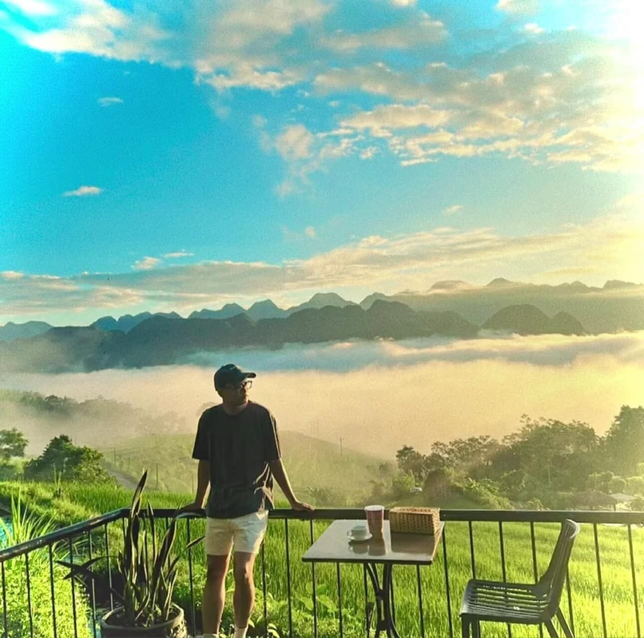 A person standing on a balcony overlooking a misty landscape with mountains in the distance.