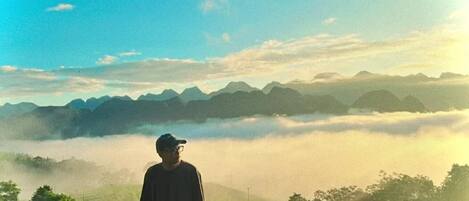 Una persona de pie en un balcón con vista a un paisaje brumoso y montañas a lo lejos.