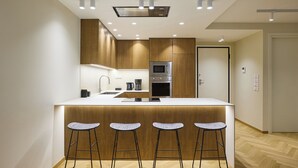 A modern kitchen with a central island, bar stools, and built-in appliances. - The Samirah Luxury Residence C4 (Elliniko - Argiroupoli)