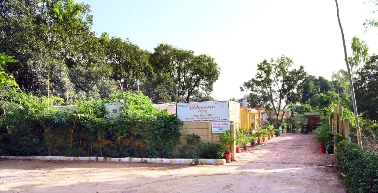 A hotel entrance with a signboard, surrounded by greenery and potted plants.