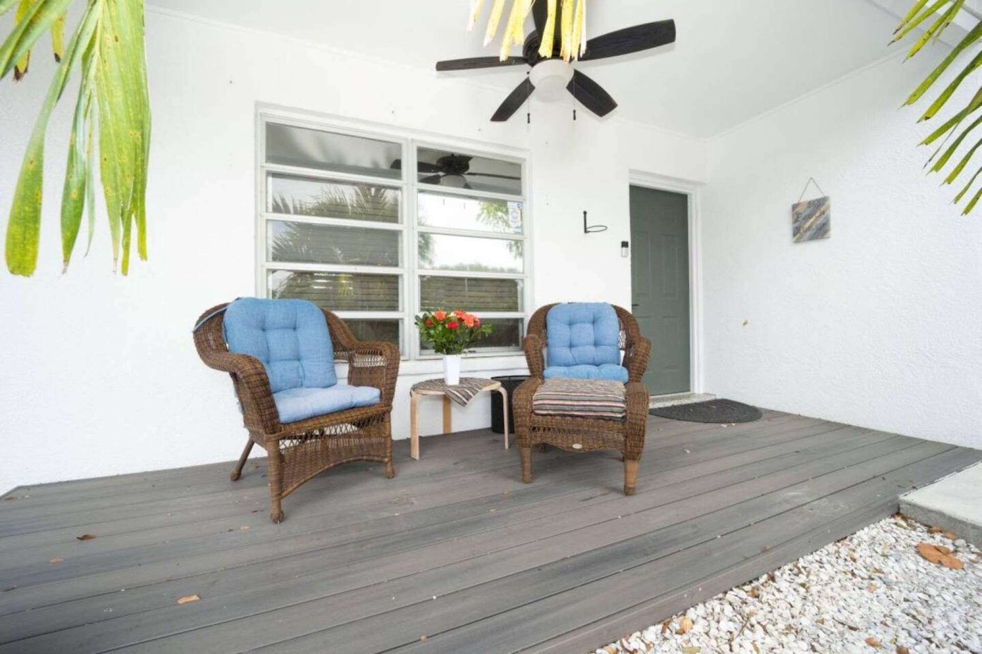 A porch with two wicker chairs, a small table, and a potted plant.