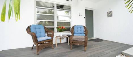 A porch with two wicker chairs, a small table, and a potted plant.