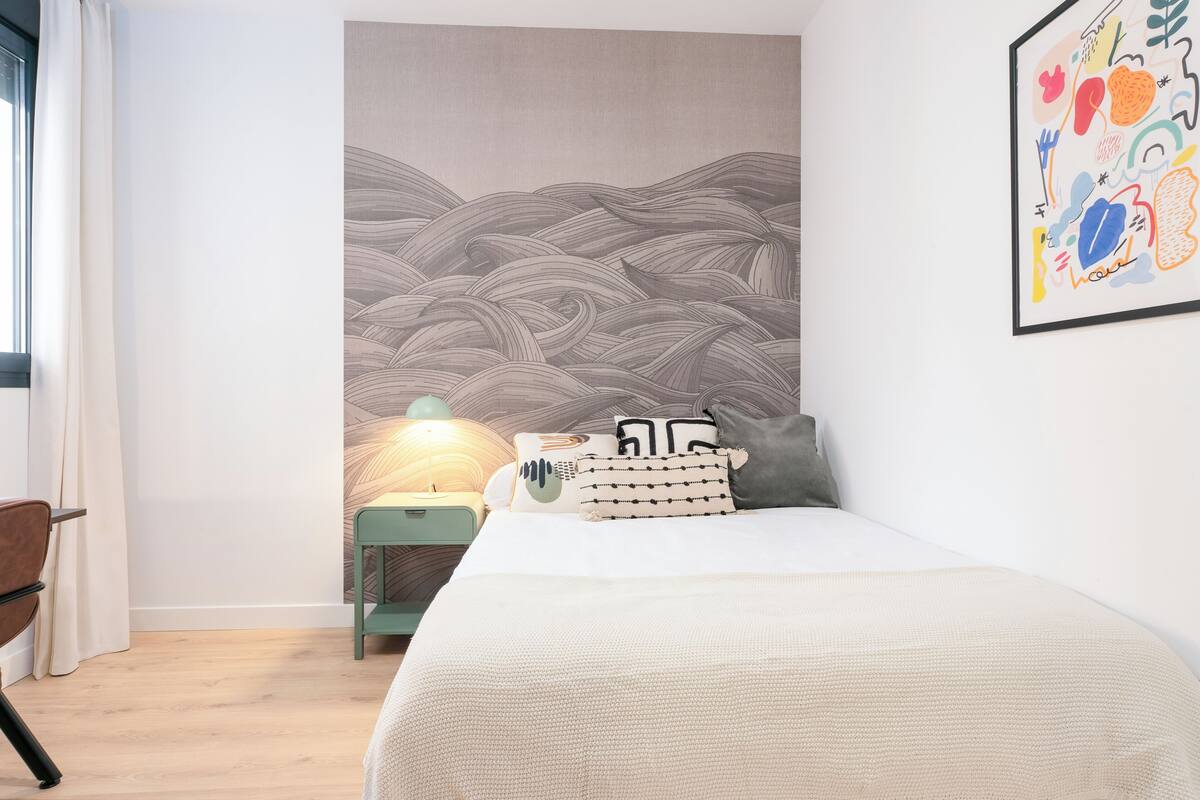 A bedroom with a bed, a nightstand, a lamp, and a wall mural.