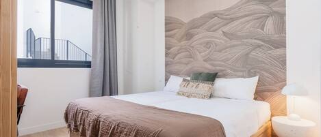 A bedroom with a large bed, a view of a building outside, and a wall with a wave pattern.