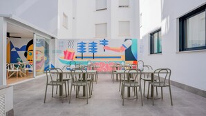 A modern dining area with tables and chairs, a colorful mural on the wall, and a building with windows and a door. - Live it Malaga (Málaga)
