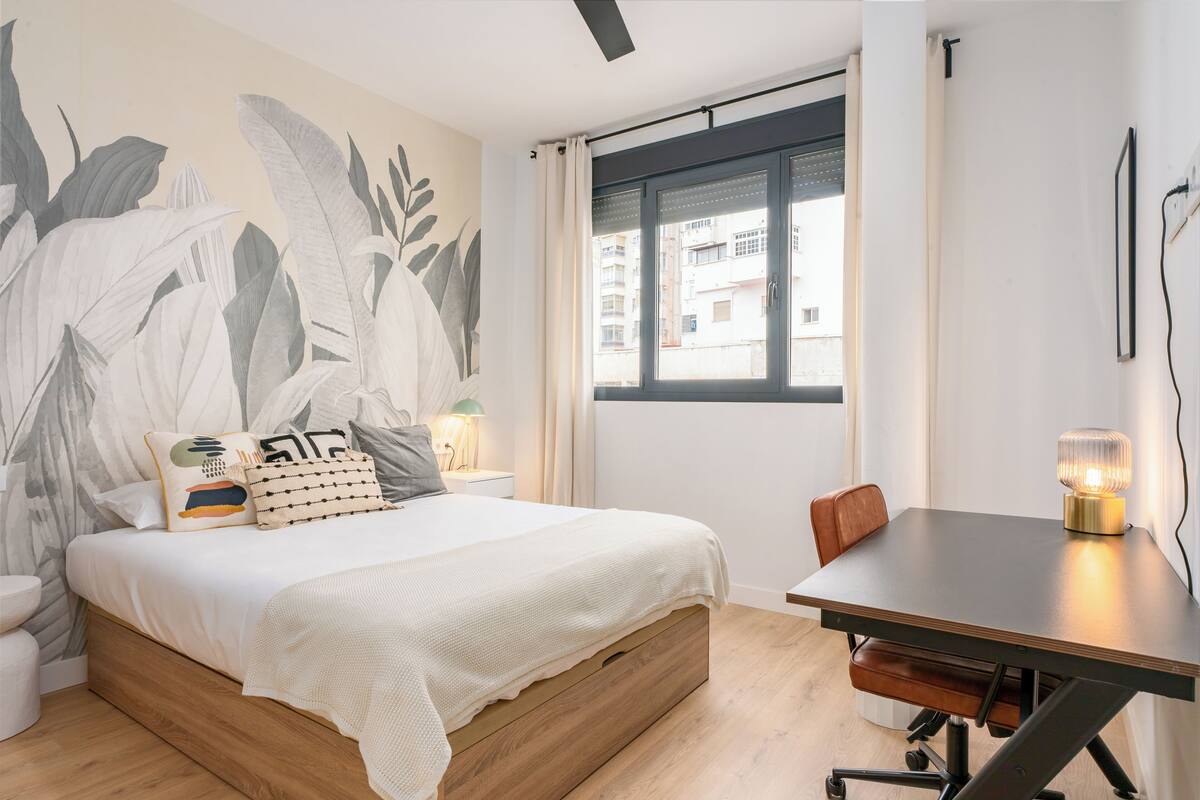 A bedroom with a bed, a desk, and a window.