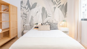 A bedroom with a bed, a wooden wardrobe, a nightstand with a lamp, and a wall mural. - Live it Malaga (Málaga)