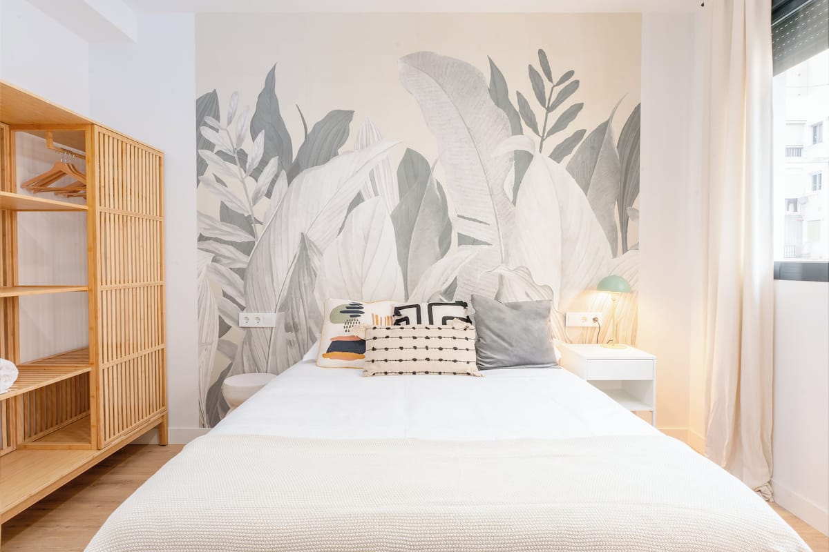 A bedroom with a bed, a wooden wardrobe, a nightstand with a lamp, and a wall mural.