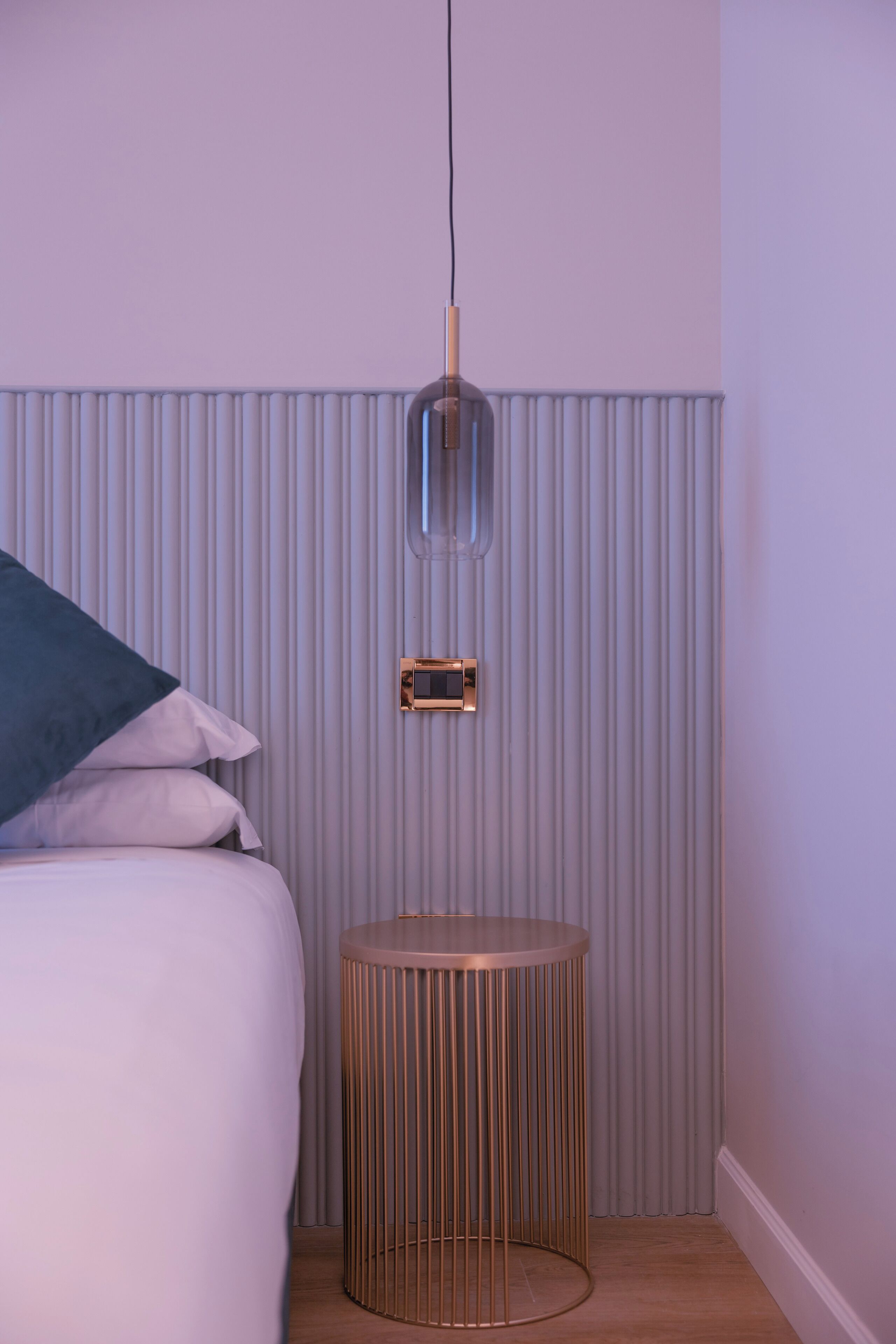 Une chambre à coucher comprenant un lit, une petite table ronde, un luminaire fixé au mur et un thermostat.
