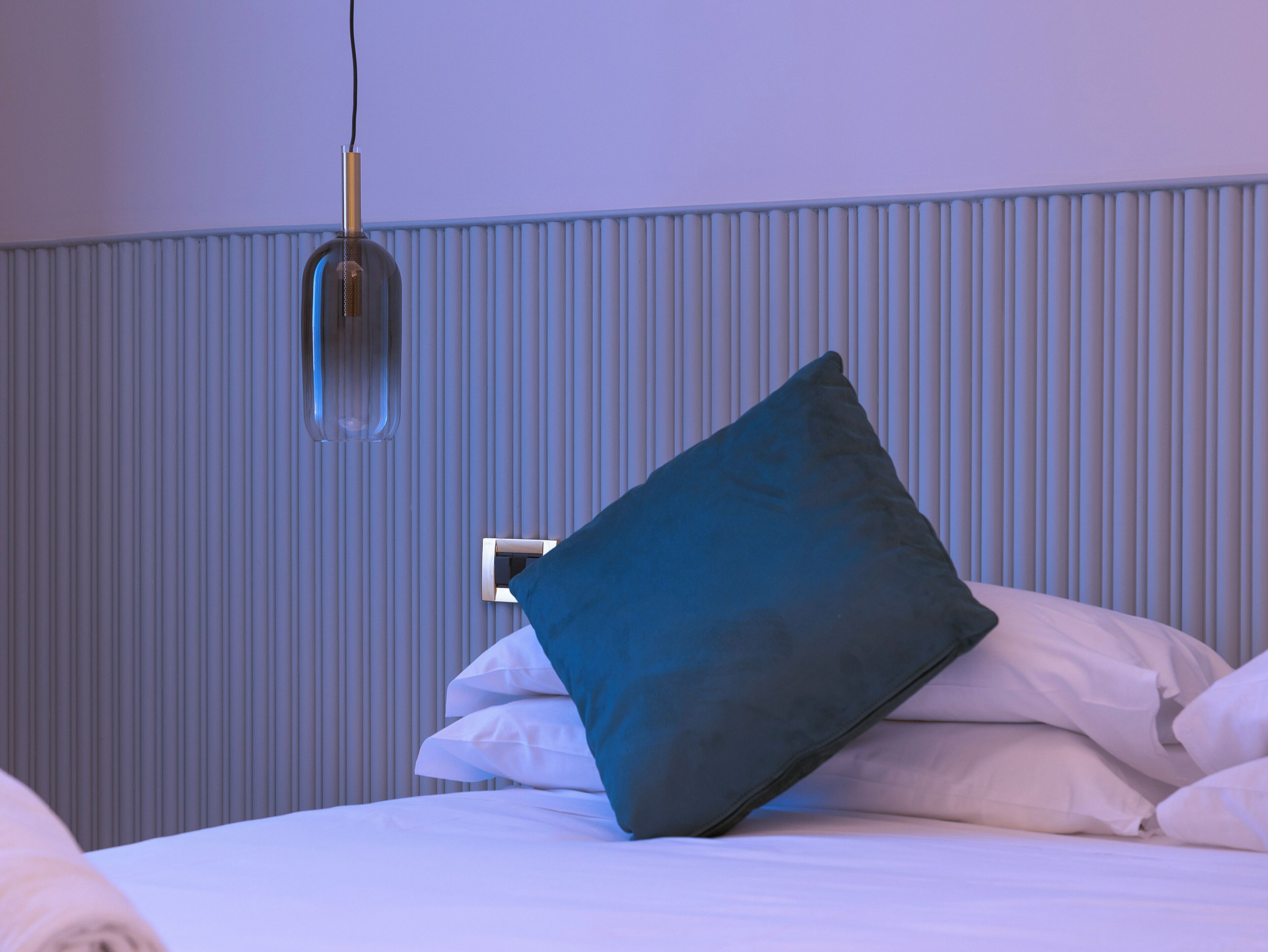 Un lit bien fait, avec des draps blancs et un seul oreiller bleu.