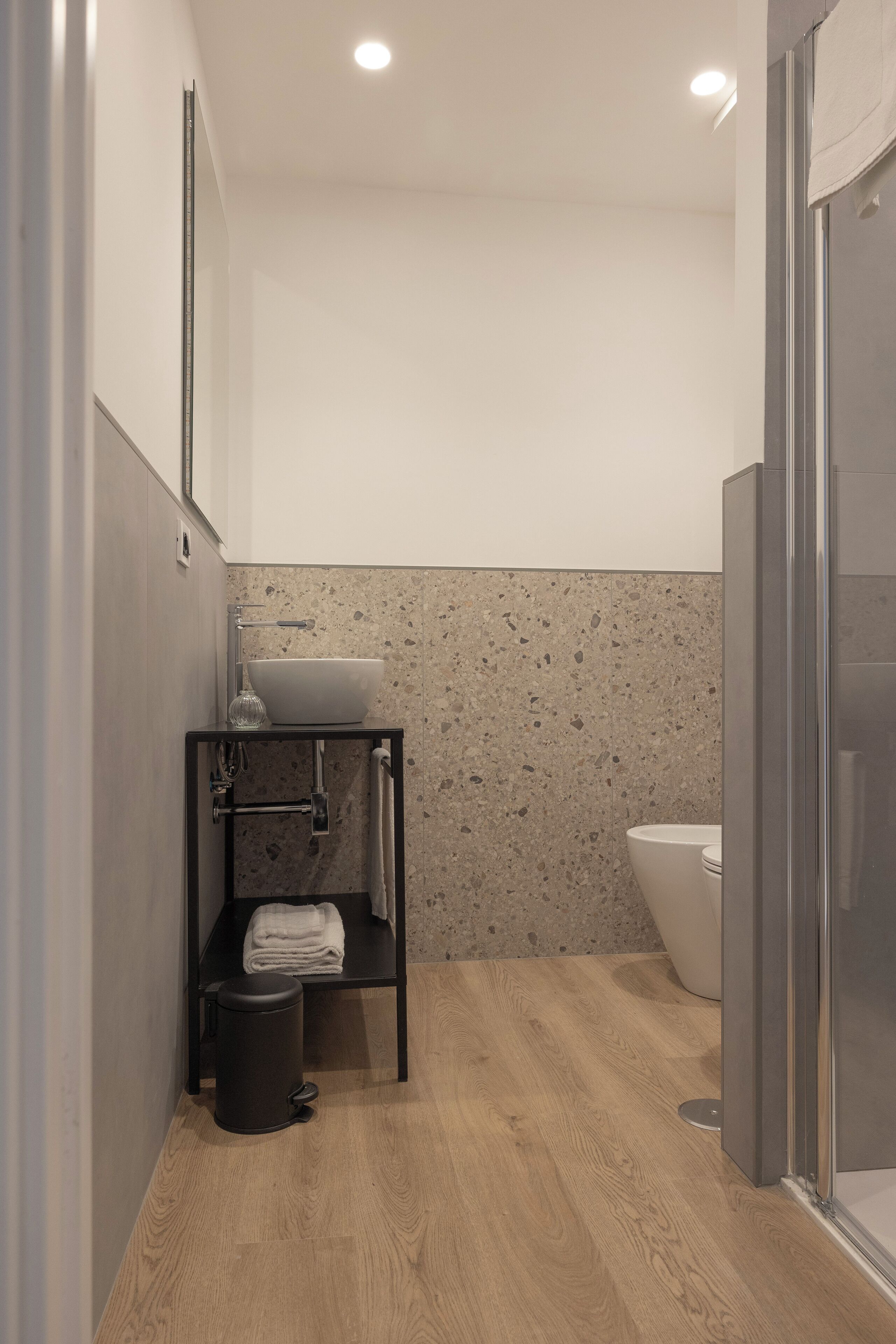 Een moderne badkamer met houten vloer, een witte wastafel, een douchecabine van glas en een handdoekrek.