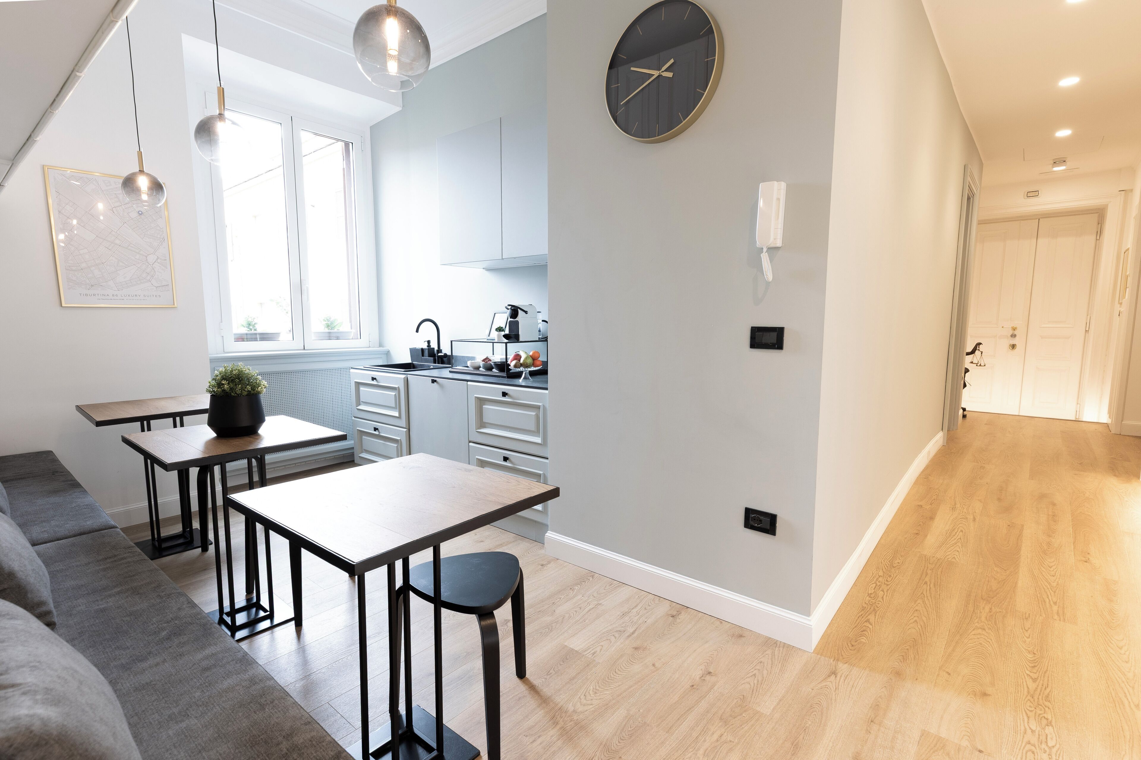 A modern kitchen with a dining area, a large wall clock, and a hallway leading to a door.