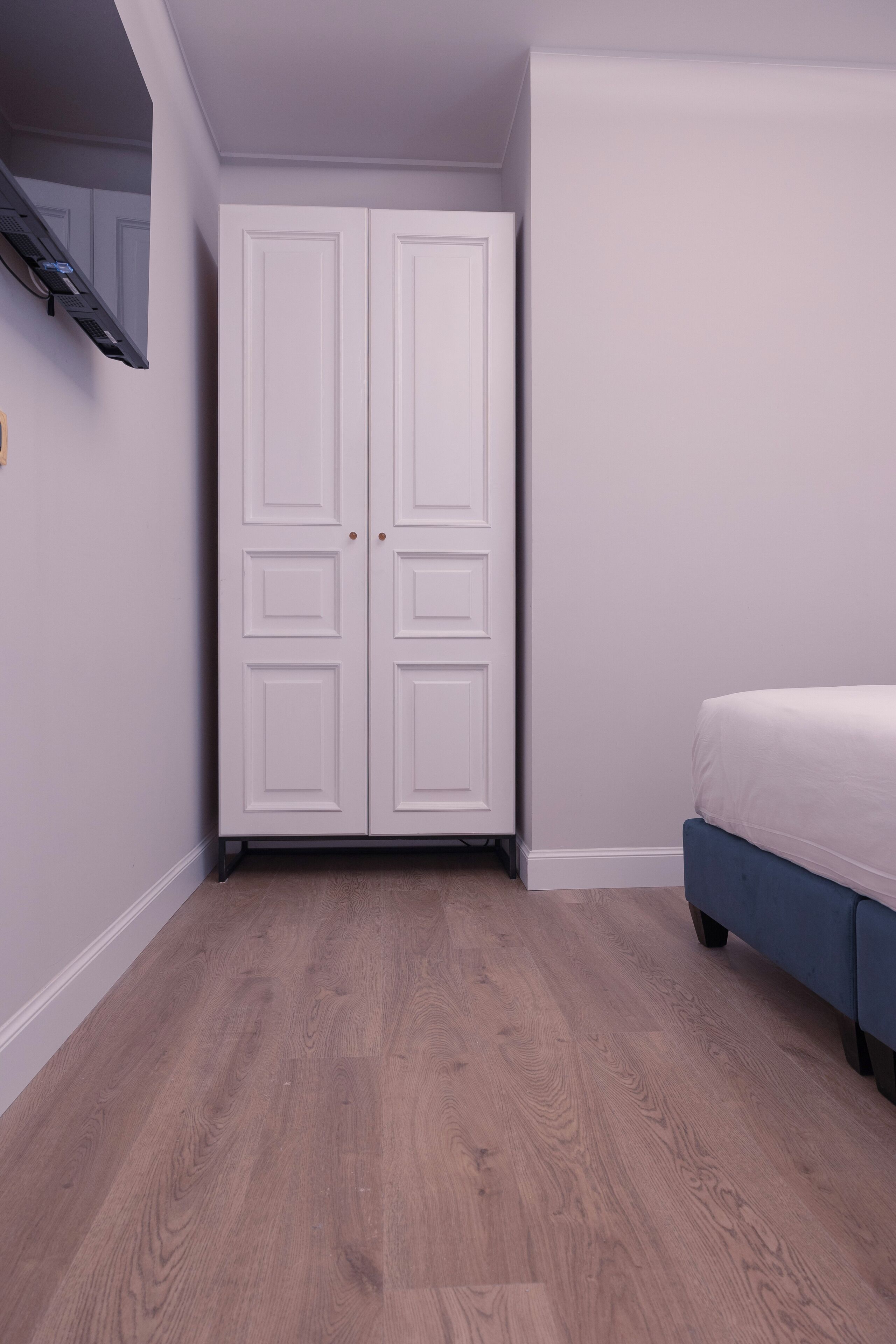 Un dormitorio con suelo de madera, una cama y un armario blanco.