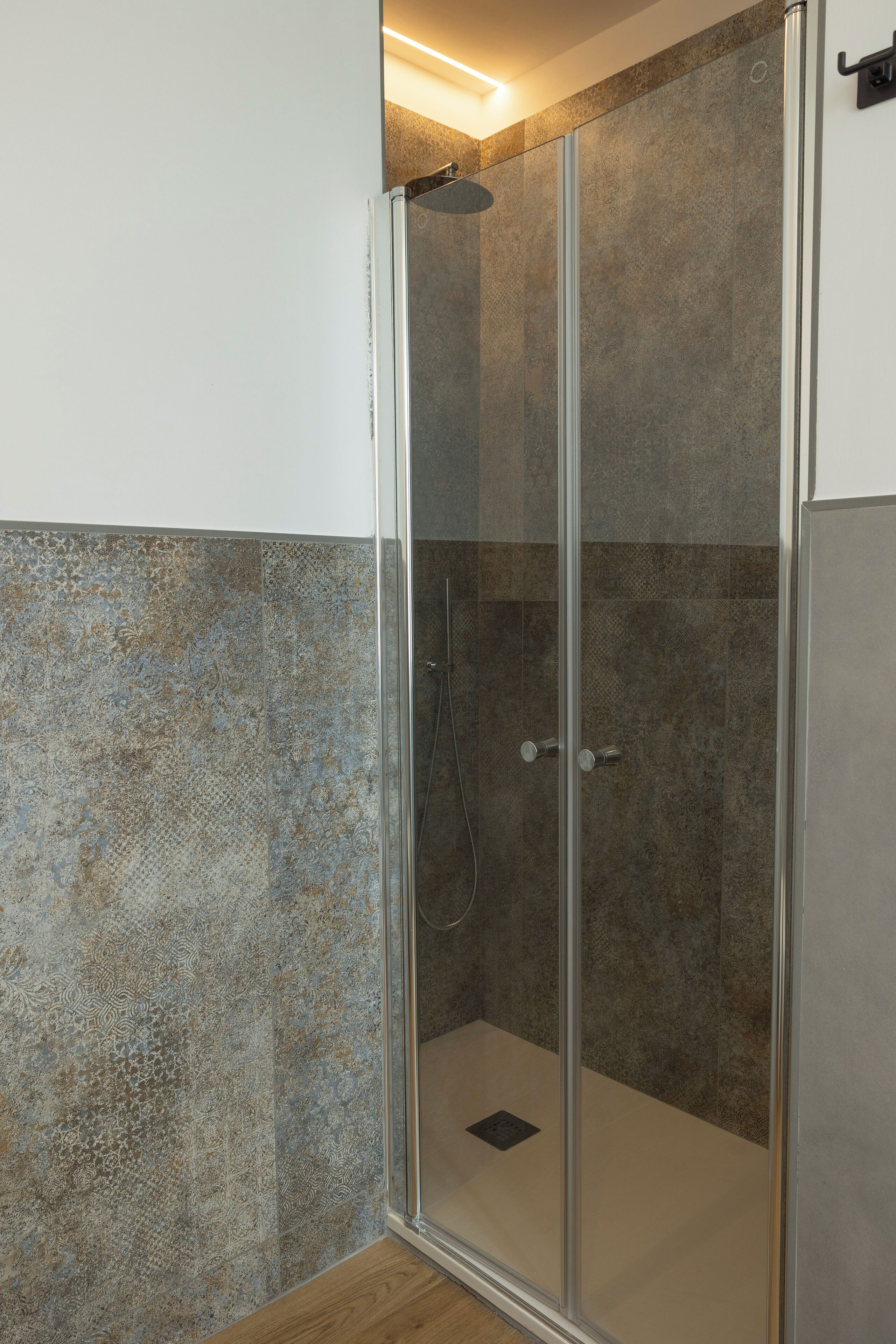 Eine gläserne Duschkabine mit Duschkopf und Bedienfeld, eine mit Fliesen versehene Wand und ein Holzboden.