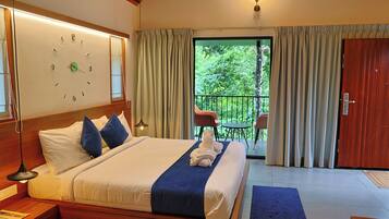 A hotel room with a large bed, a clock on the wall, a balcony with a table and chairs, and a wooden door.