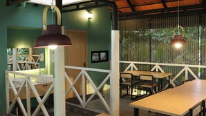 A restaurant with long wooden tables and hanging pendant lights. - Bay View Suites Vythiri (Vythiri)