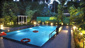 A rectangular swimming pool with lifebuoys, surrounded by a garden with trees and plants, and a covered seating area. - Bay View Suites Vythiri (Vythiri)