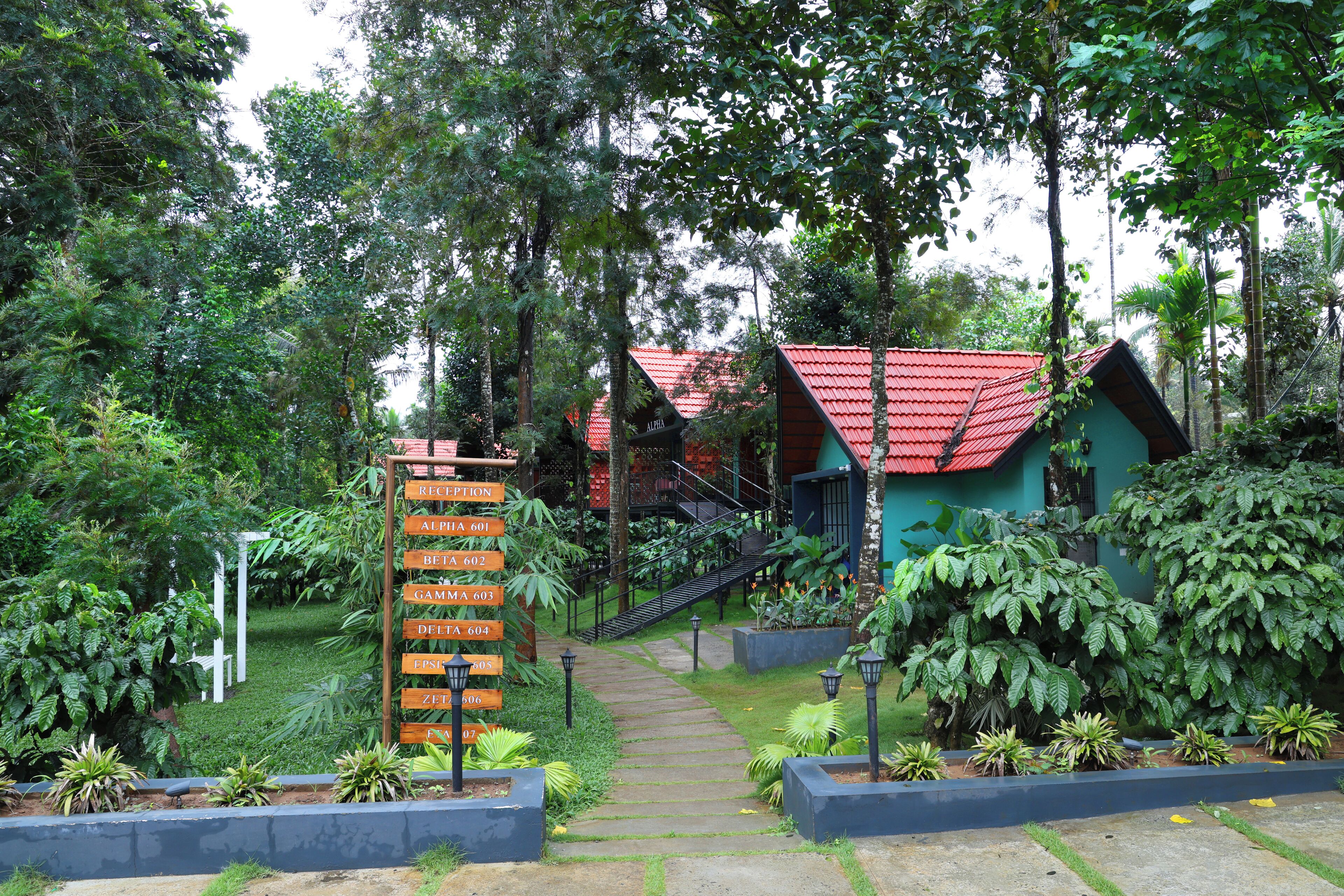 A pathway leading to a building with a red roof, surrounded by lush greenery and a signpost with room numbers.