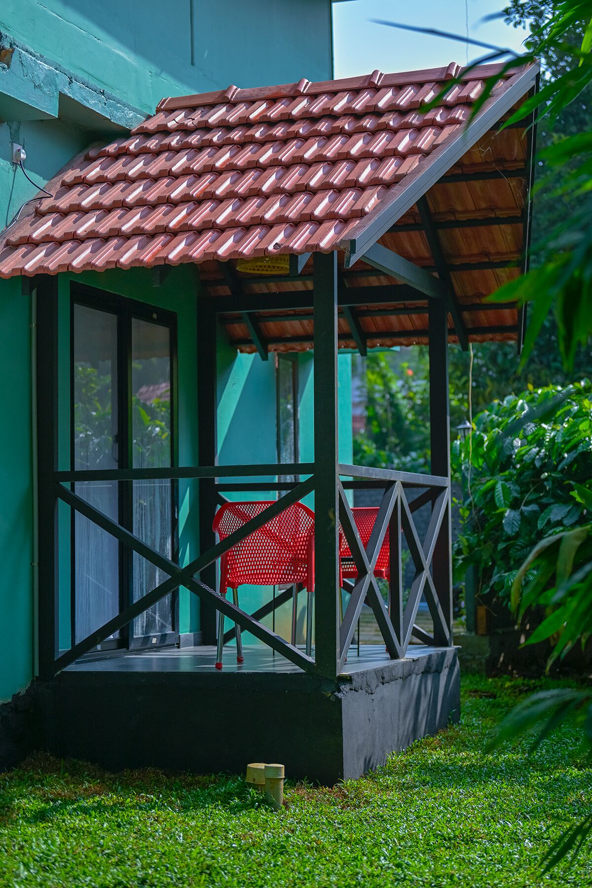 A small, green house with a tiled roof and a covered porch.