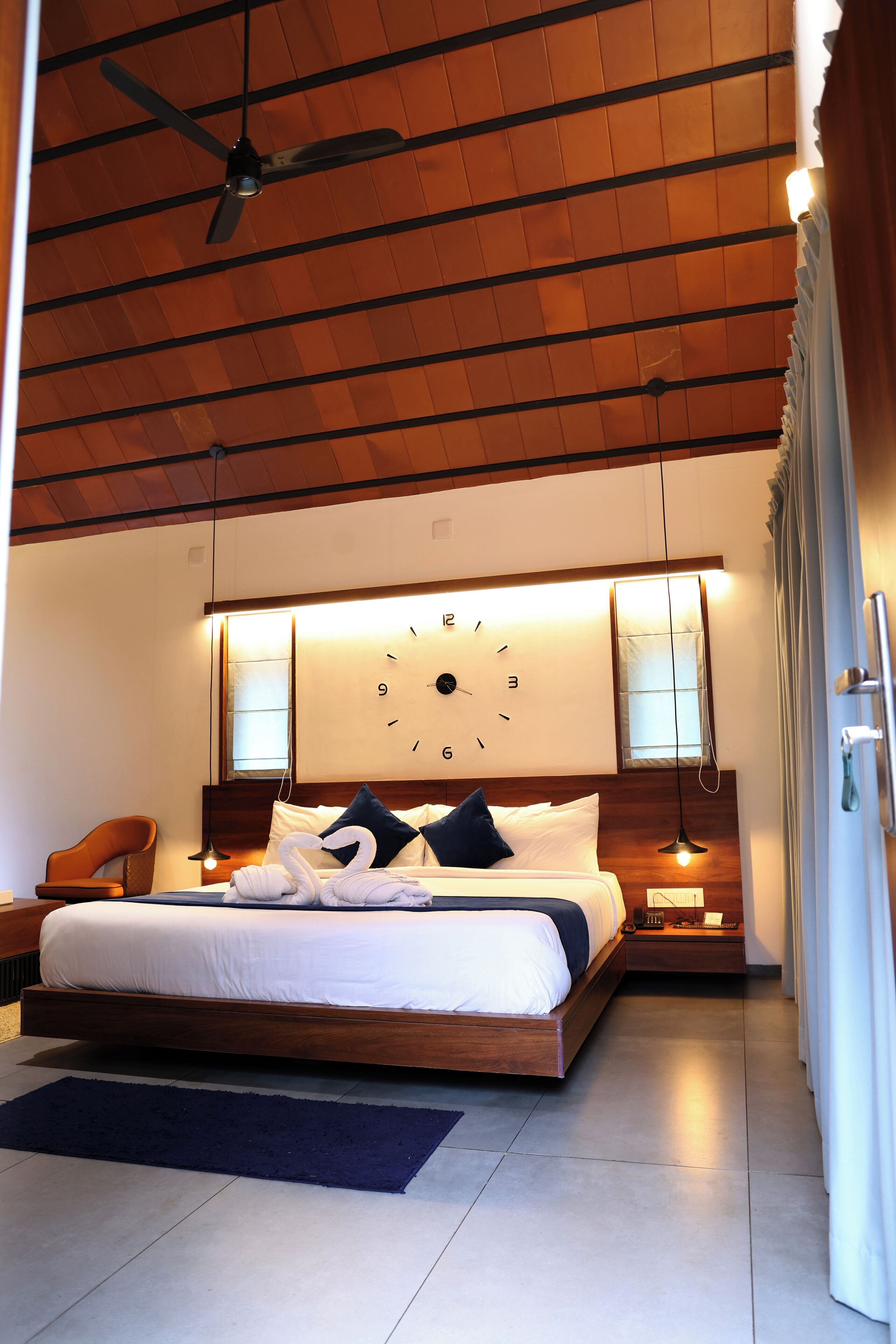 Een moderne slaapkamer met een groot bed, een plafondventilator, een wandklok en een nachtkastje met een lamp.