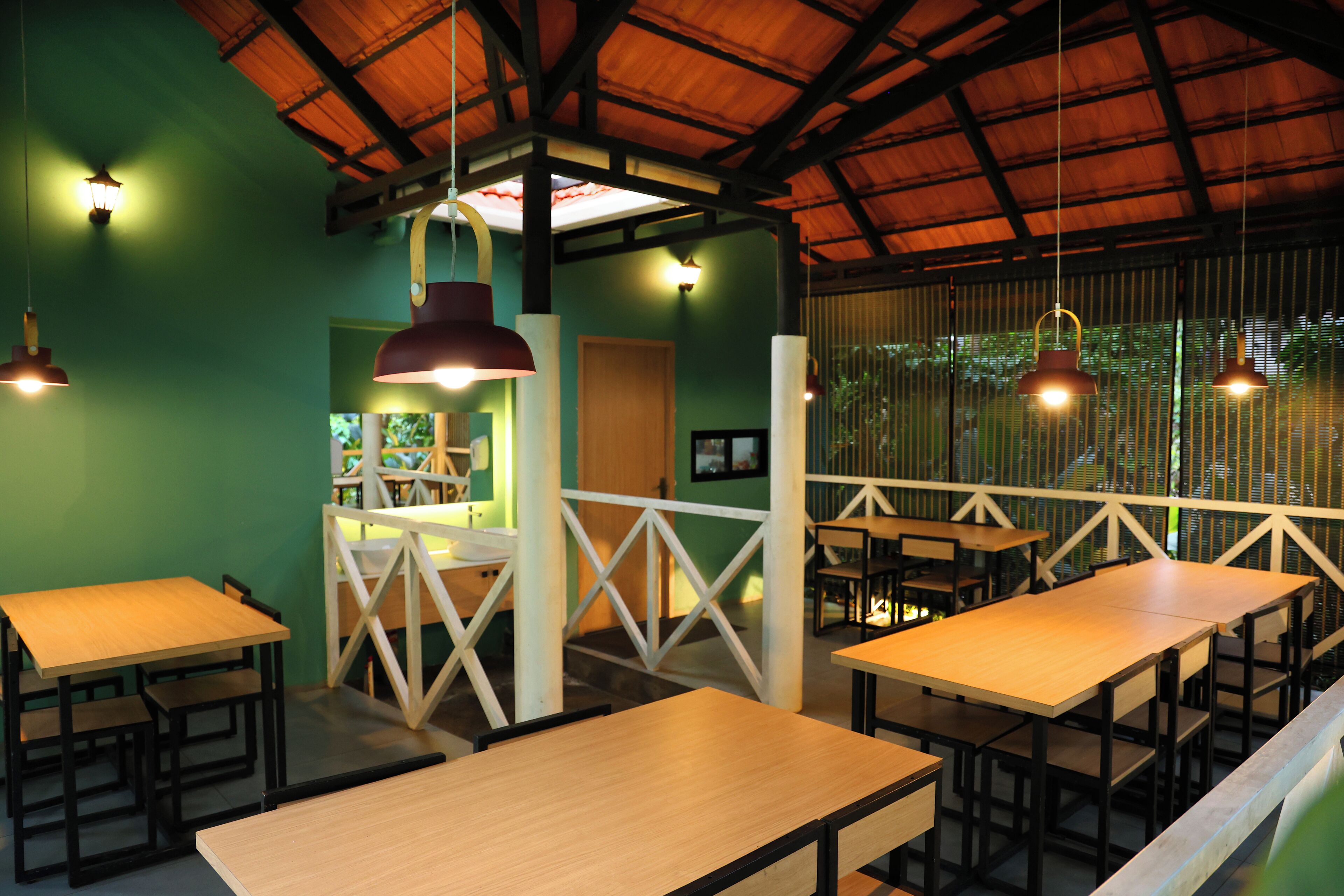 A restaurant with wooden tables and chairs, hanging pendant lights, and a green wall.