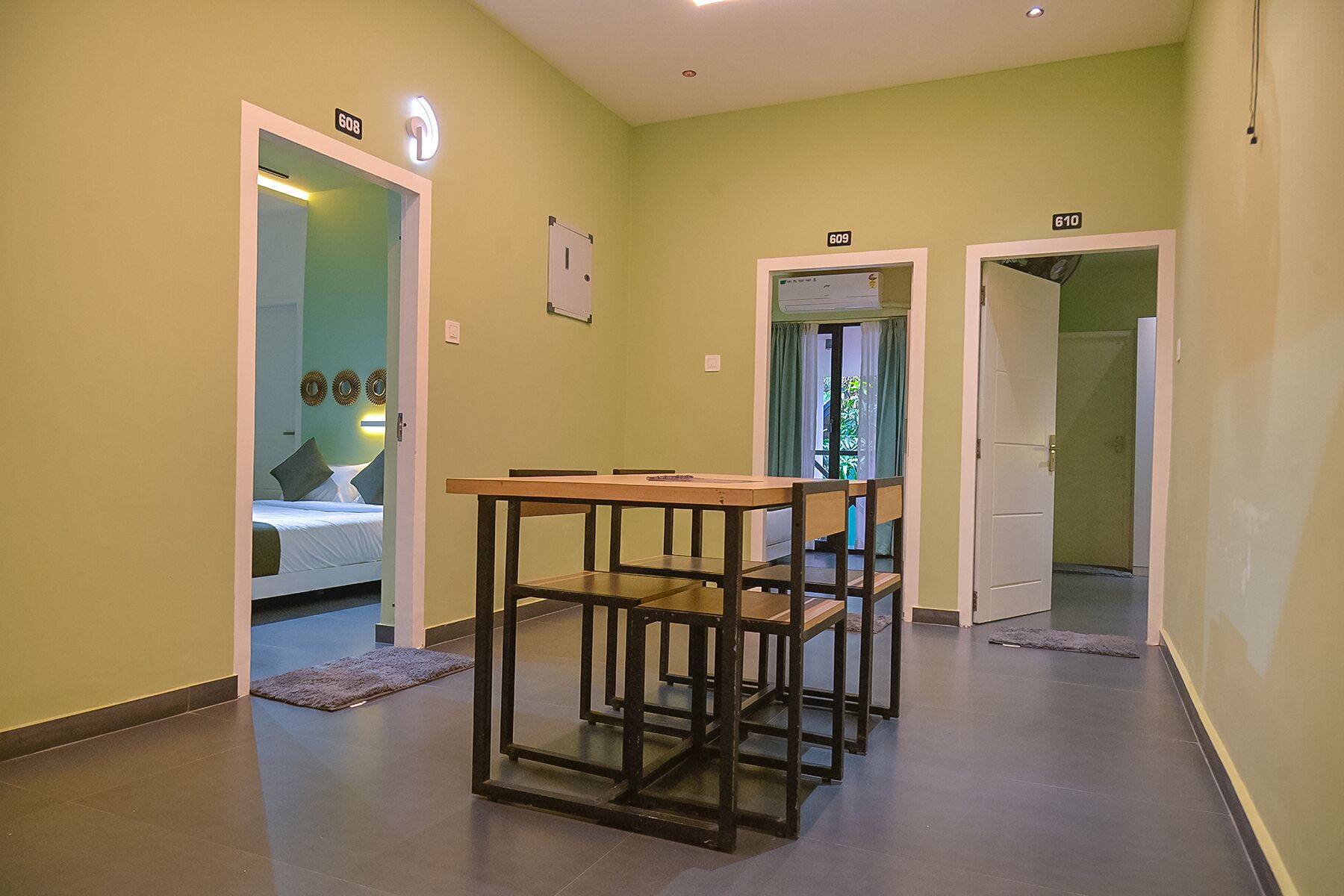 Un pasillo con una mesa de comedor y sillas, una cama en la habitación contigua, y puertas con los números 608, 609 y 610.