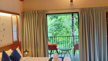Een slaapkamer met een groot bed, een plafondventilator, uitzicht op groen en een balkon met stoelen.