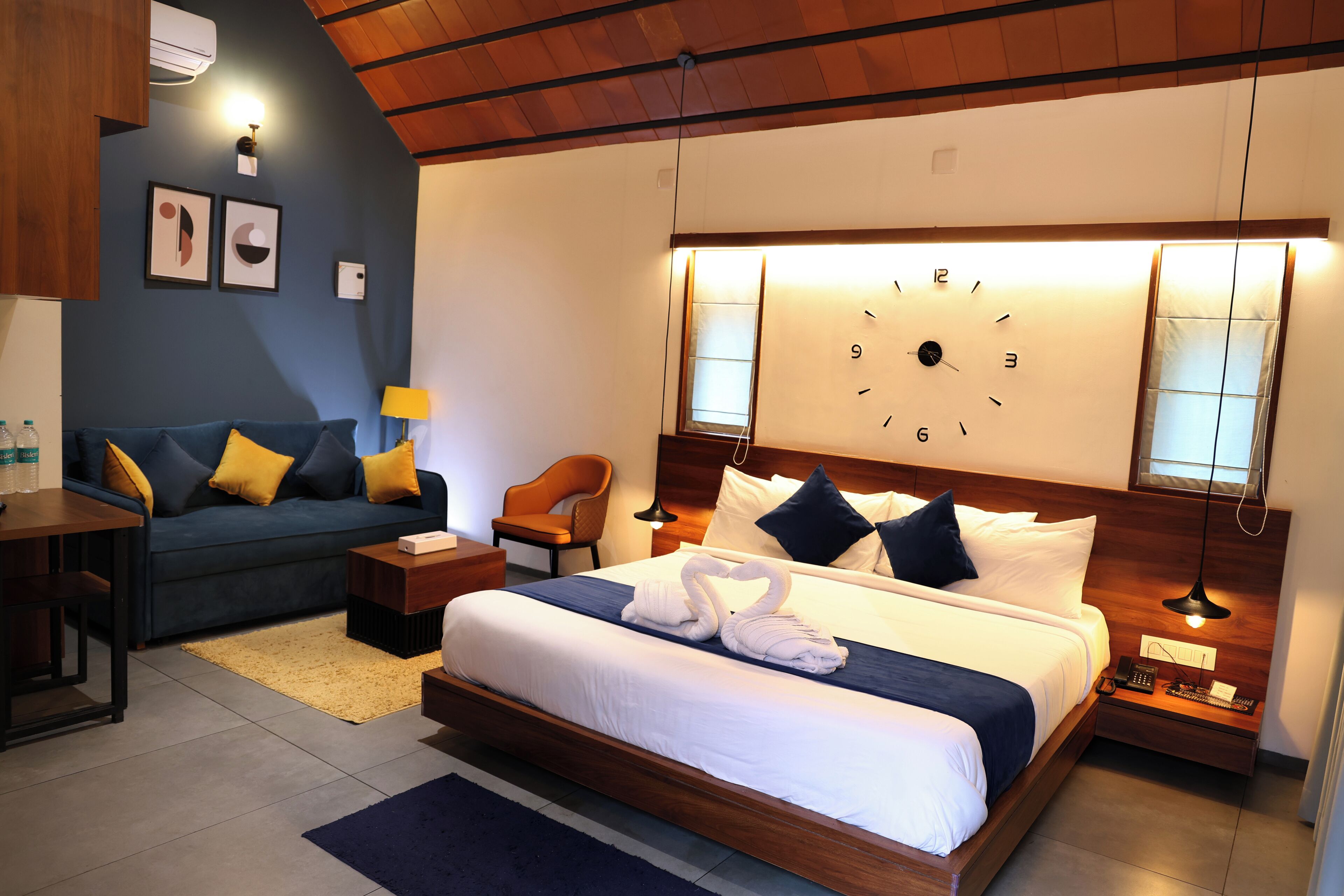 A hotel room with a large bed, a sofa, a desk, and a nightstand with a lamp.