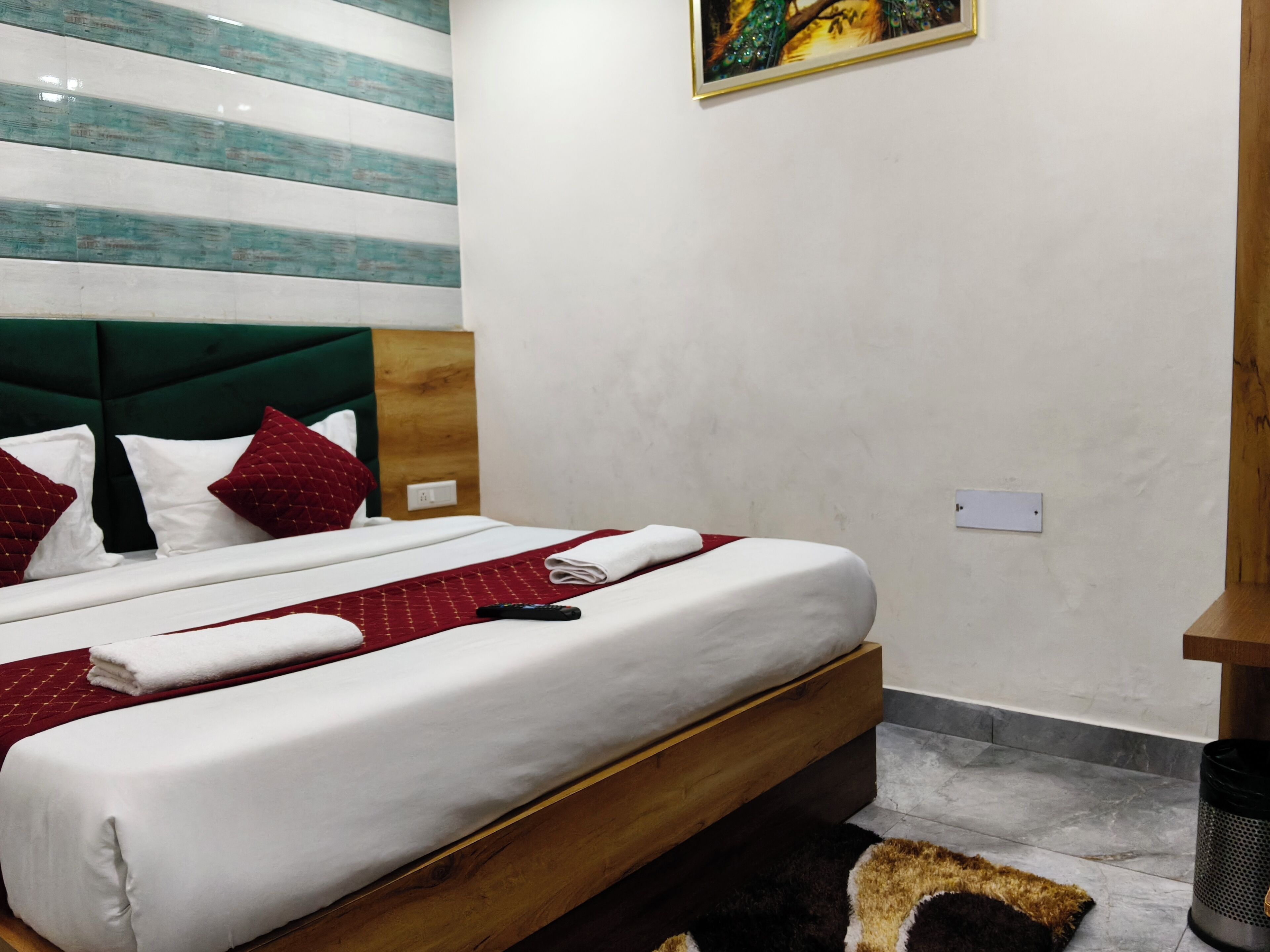 A neatly made bed with white and red bedding, a wooden headboard, and a painting on the wall.