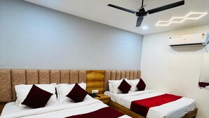 A hotel room with two beds, a ceiling fan, recessed lighting, and an air conditioning unit. - Hotel Bella Vista Inn (Amritsar)