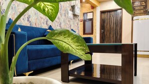 A modern living room with a blue sofa, a glass-top coffee table, and a potted plant. - Hotel Bella Vista Inn (Amritsar)