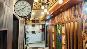 A reception area with a clock, reception desk, and potted plants. - Hotel Bella Vista Inn (Amritsar)