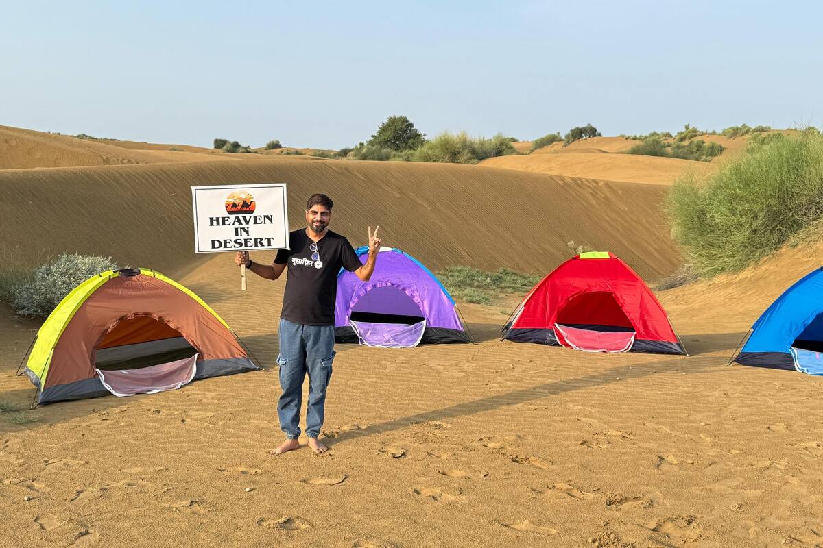 Una persona in piedi di fronte a diversi tende colorate in un paesaggio desertico, con dune di sabbia sullo sfondo.