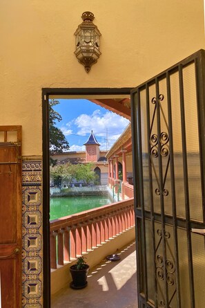 Vista a través de una puerta abierta con un farol decorativo encima, que da a un patio con fuente y un edificio con torre.