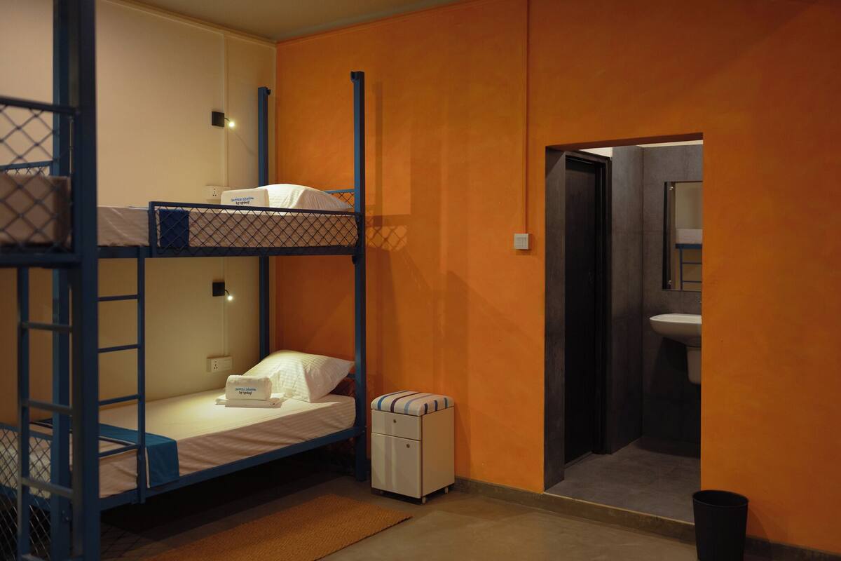Ein Schlafraum mit Etagenbetten, einem kleinen Nachttisch und einem Badezimmer mit Waschbecken.