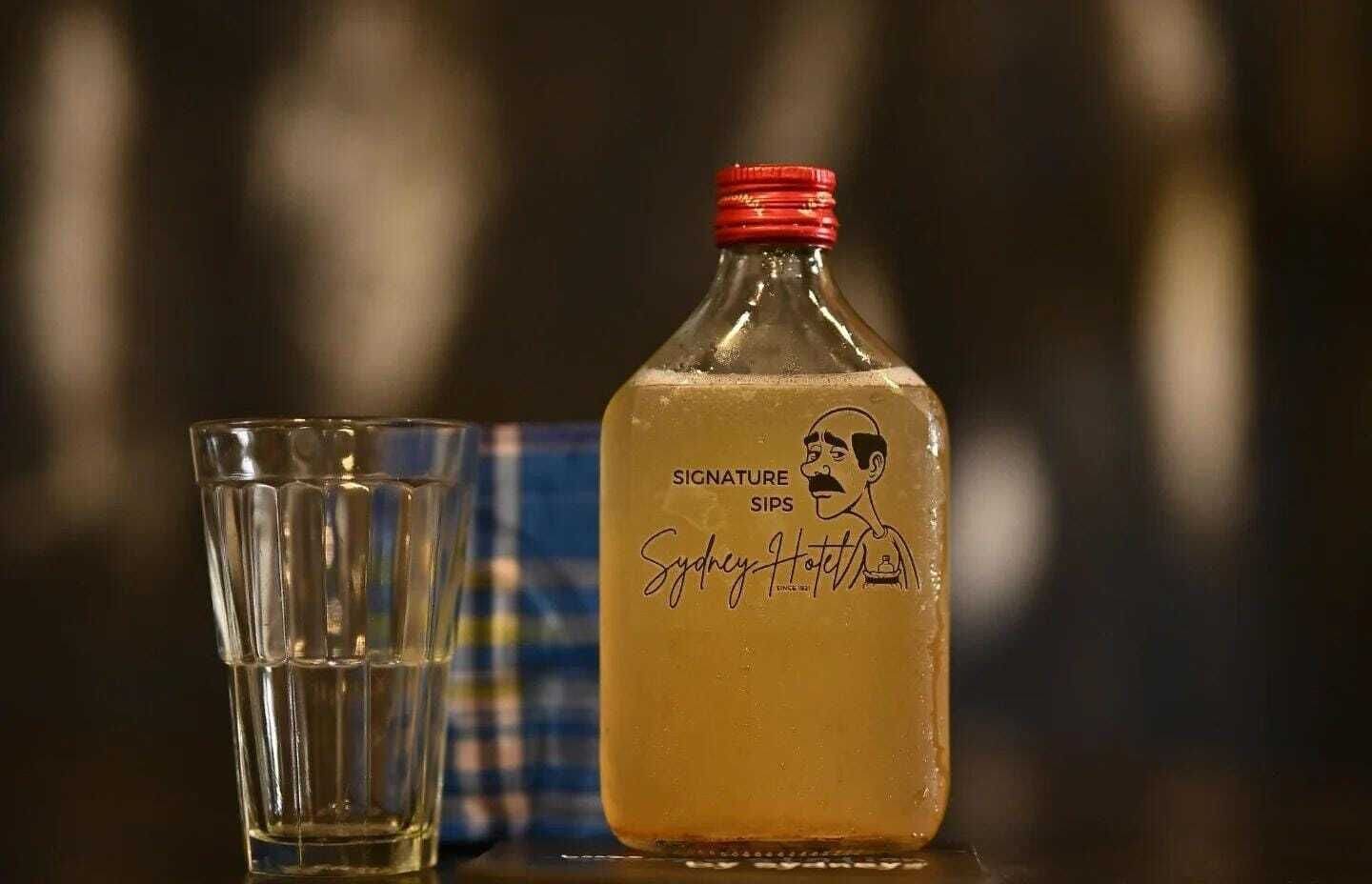 A bottle of signature sips with a red cap and a glass beside it.