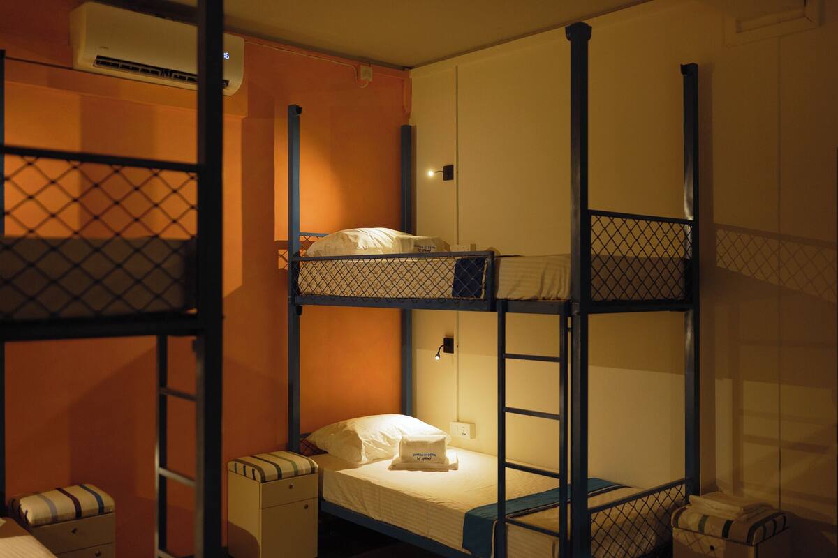 Ein Mehrbettzimmer mit einem Einzelbett und einem darüber liegenden Schlafplatz. Ein kleiner Nachttisch und ein Stuhl sind ebenfalls vorhanden.