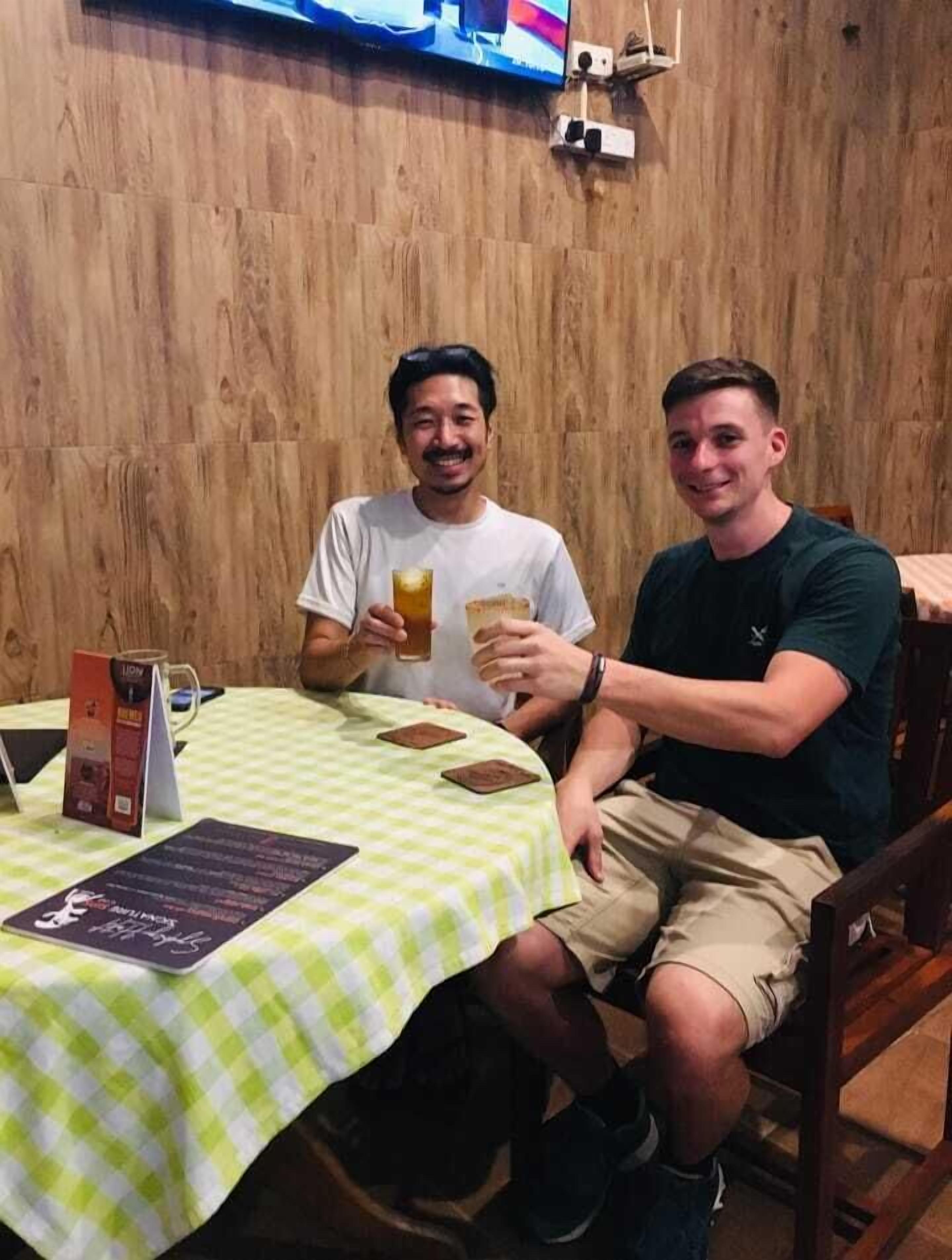 Two people sitting at a table with a checkered tablecloth, holding drinks.