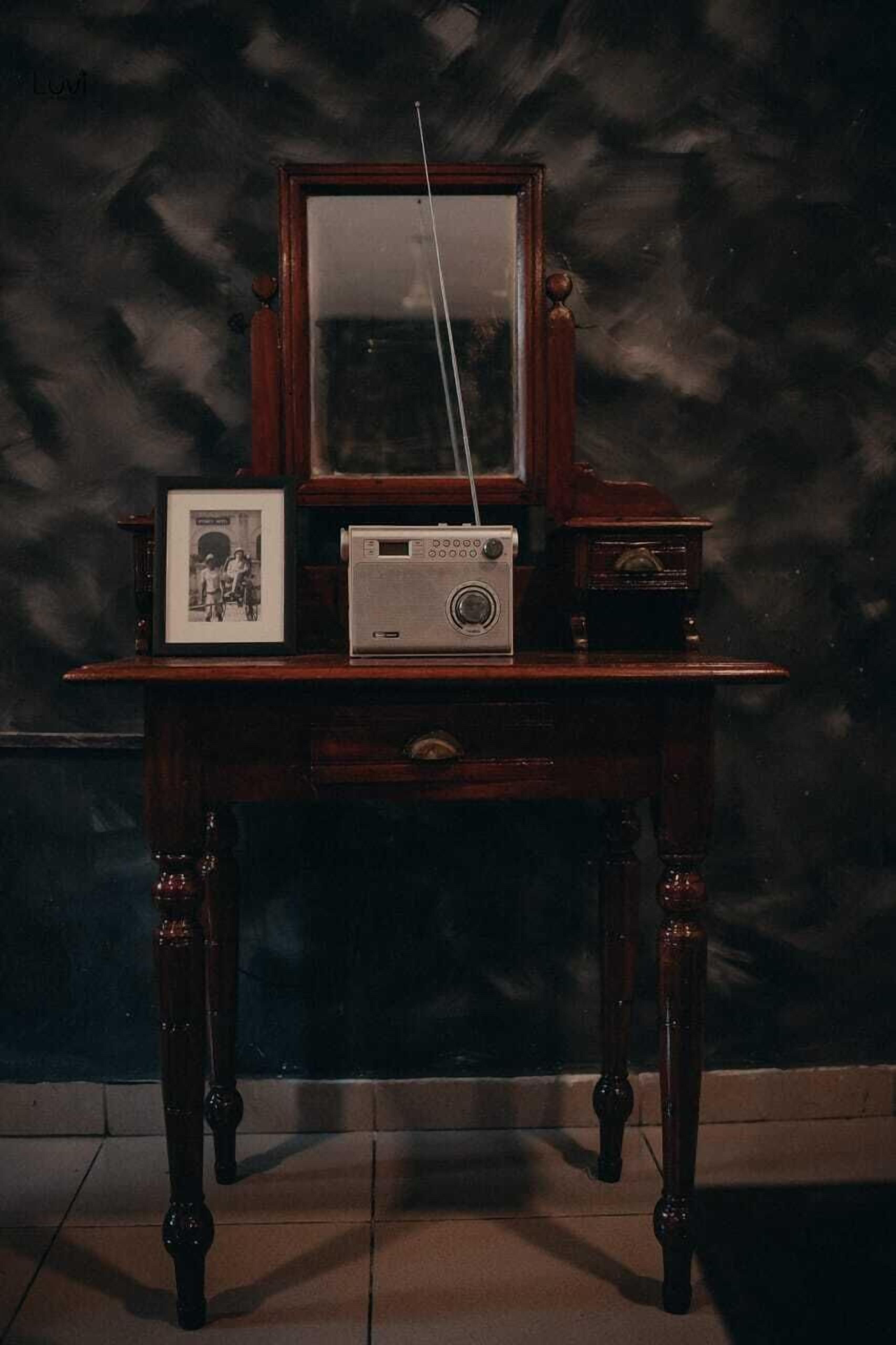 A wooden desk with a vintage radio, a framed photograph, and a mirror.