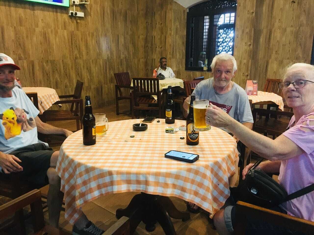 En grupp människor sitter runt ett runt bord med en rutig duk och dricker något.