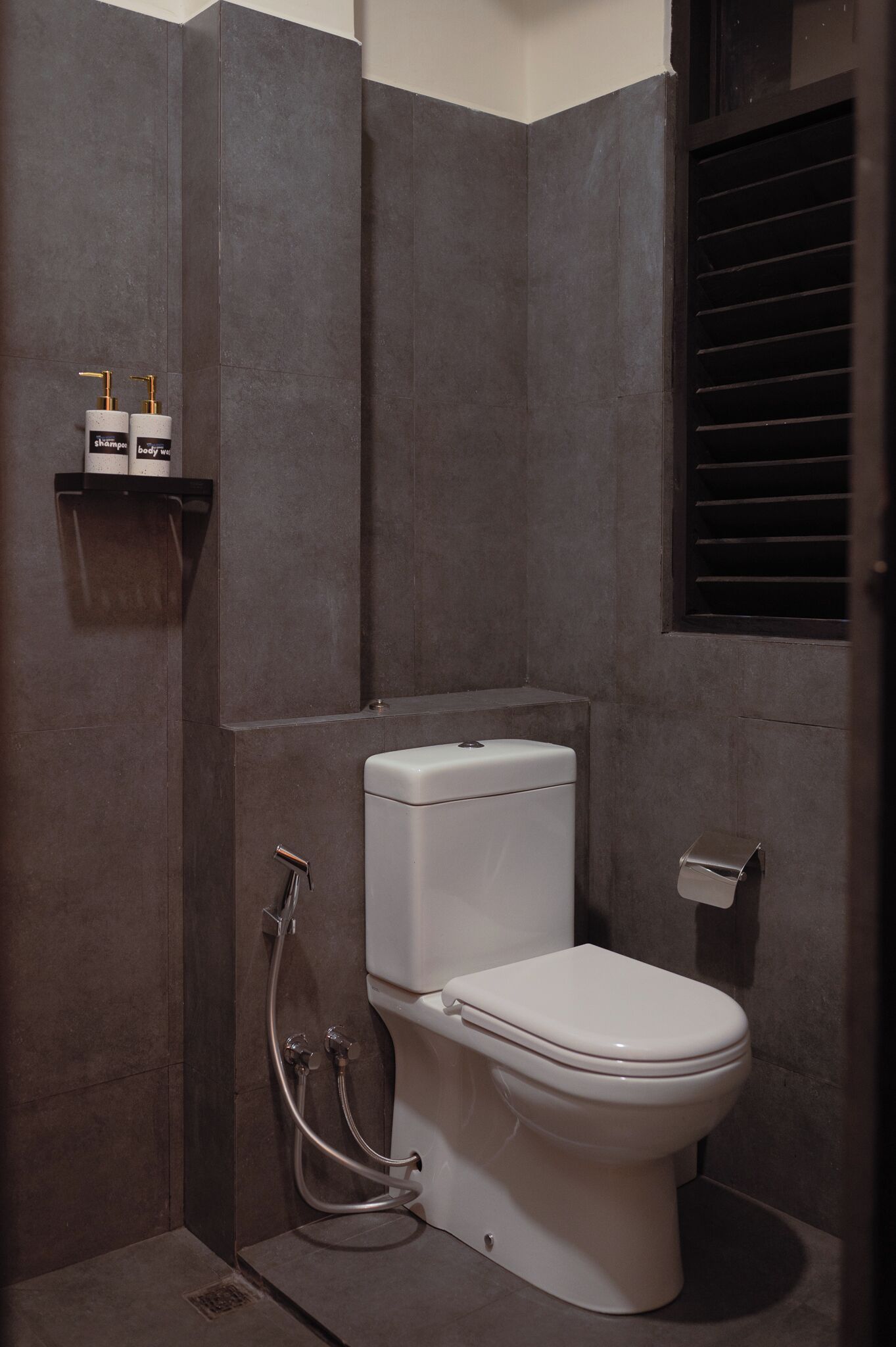 A compact bathroom with a white toilet, a shower area, and a shelf with toiletries.