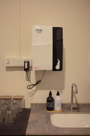 Un baño con un lavabo blanco, un espejo, un dispensador de toallas negro y dos botellas etiquetadas 'DISHES' y 'HAN'.