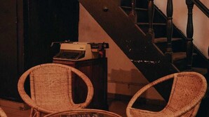 A staircase with wooden balusters, wicker chairs, and a small table with a typewriter. - Snooze Station by Sydney Galle (Galle)