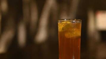 A glass of amber-colored beverage on a coaster with a blurred background.