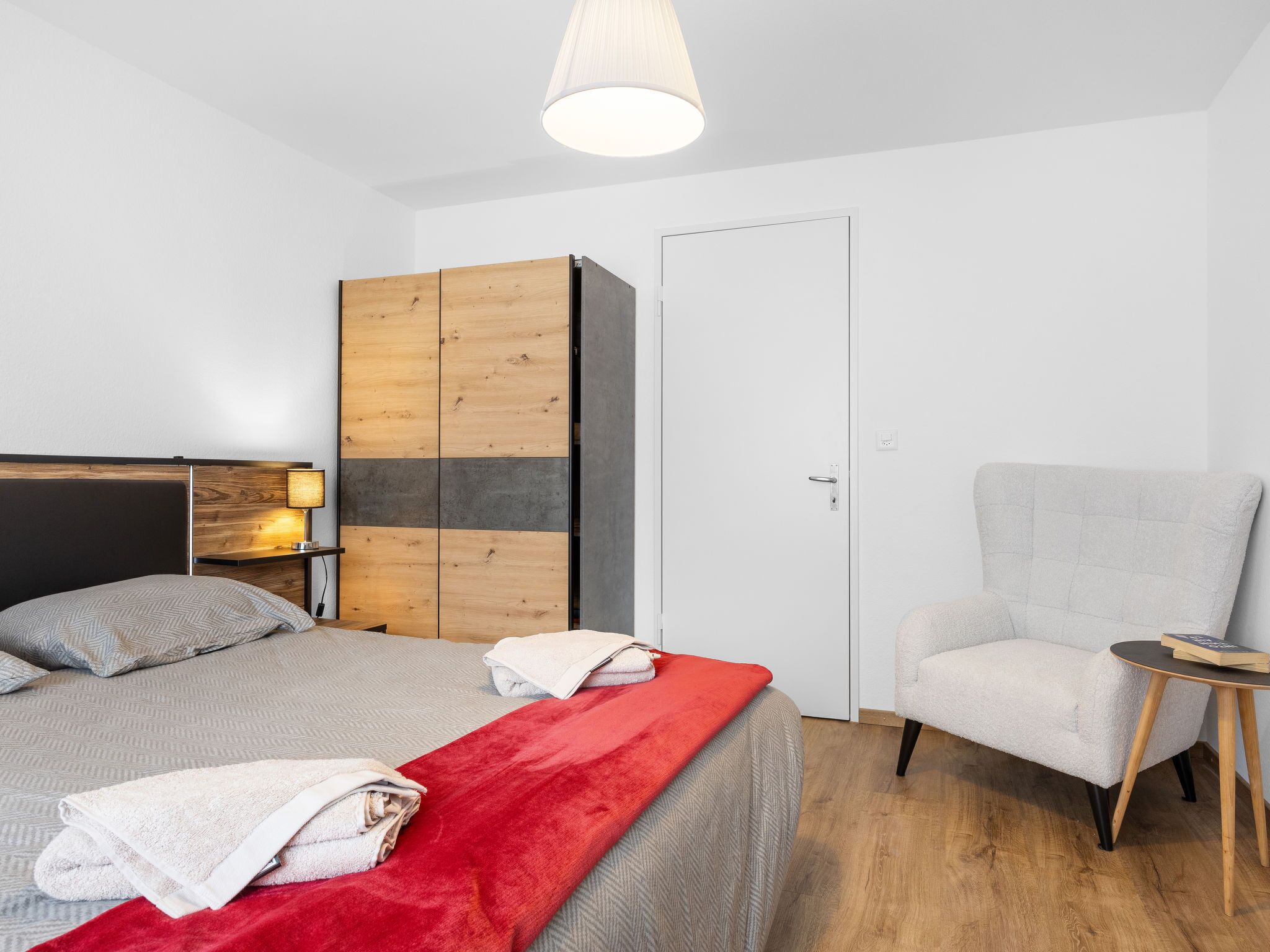 Un dormitorio moderno con cama, una silla, armario y lámpara.